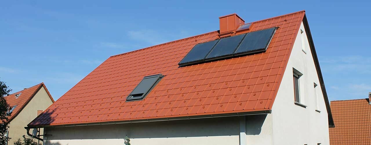 Maison individuelle avec toit à deux versants recouvert de tuiles PREFA rouge tuile. Surface de toit avec installation solaire et fenêtre de toit