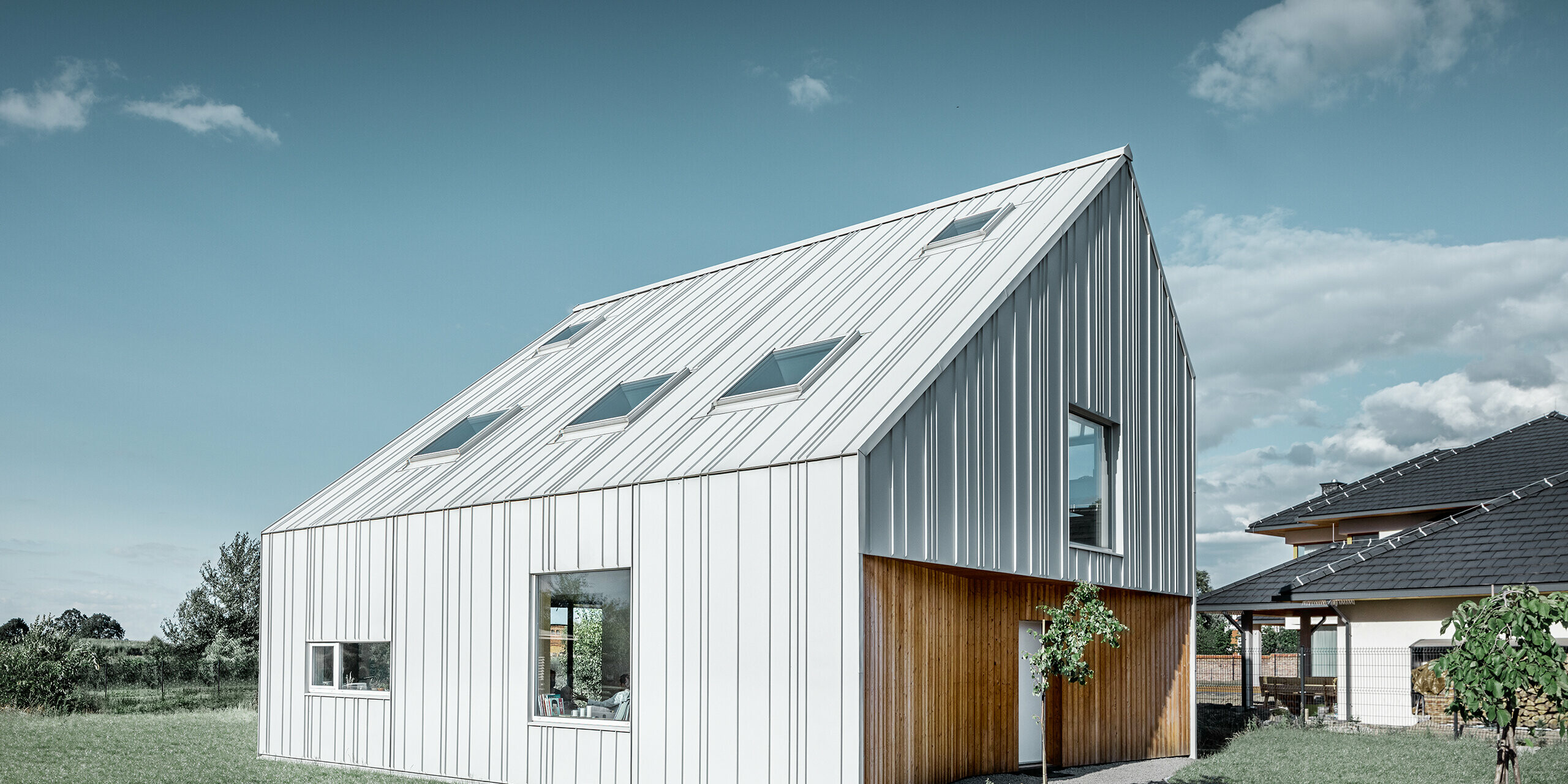 Maison individuelle moderne avec toit à pignon ; tout l’habillage extérieur a été réalisé avec PREFALZ en blanc Prefa. Les bacs de différentes largeurs s'étendent du toit à la façade. Plusieurs fenêtres de toit sont intégrées dans le toit.