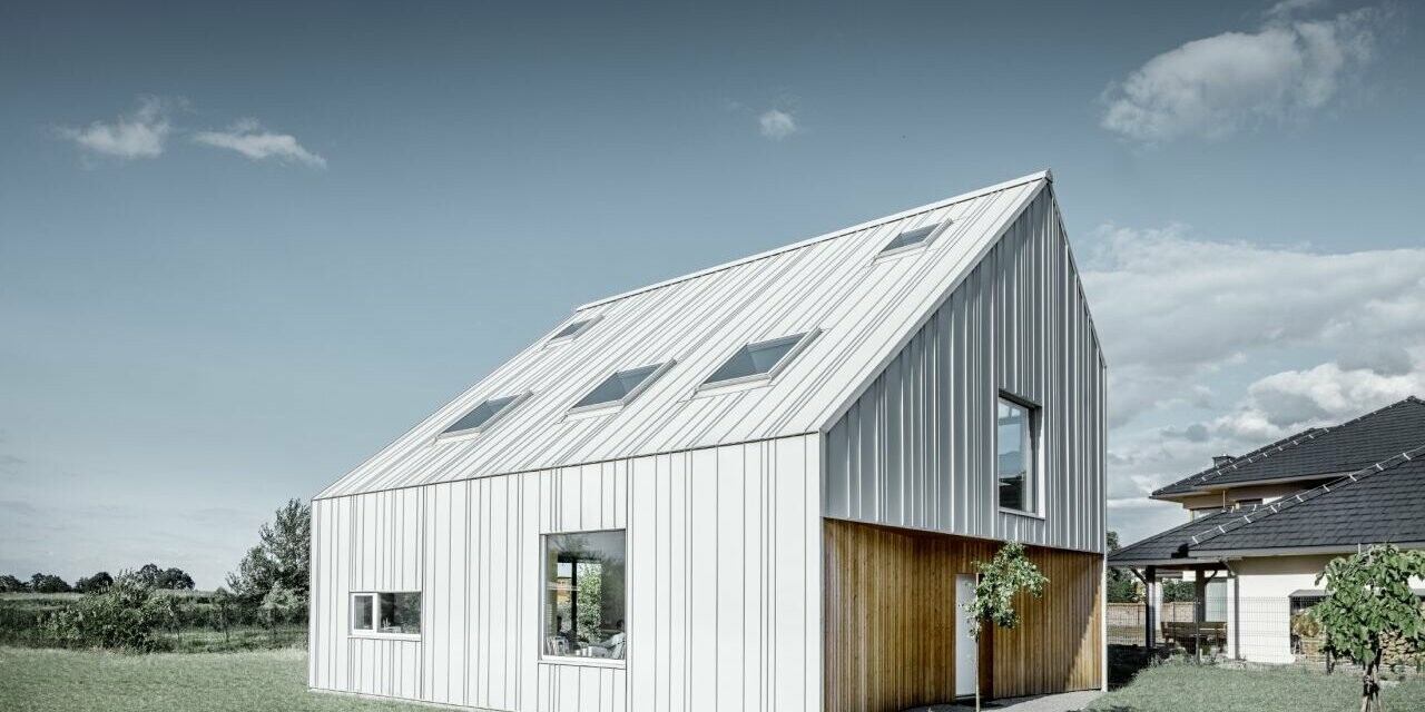 Maison individuelle moderne avec toit à pignon ; tout l’habillage extérieur a été réalisé avec PREFALZ en blanc Prefa. Les bacs de différentes largeurs s'étendent du toit à la façade. Plusieurs fenêtres de toit sont intégrées dans le toit.