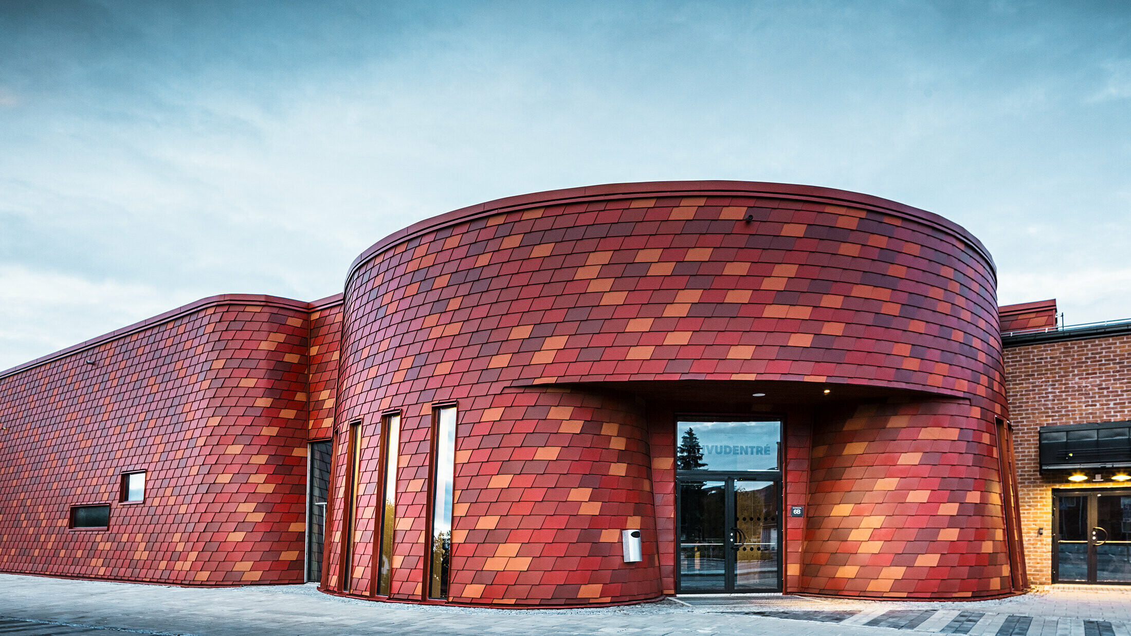 Grande patinoire à angles arrondis. La façade a été habillée de bardeaux PREFA dans différentes teintes de rouge.