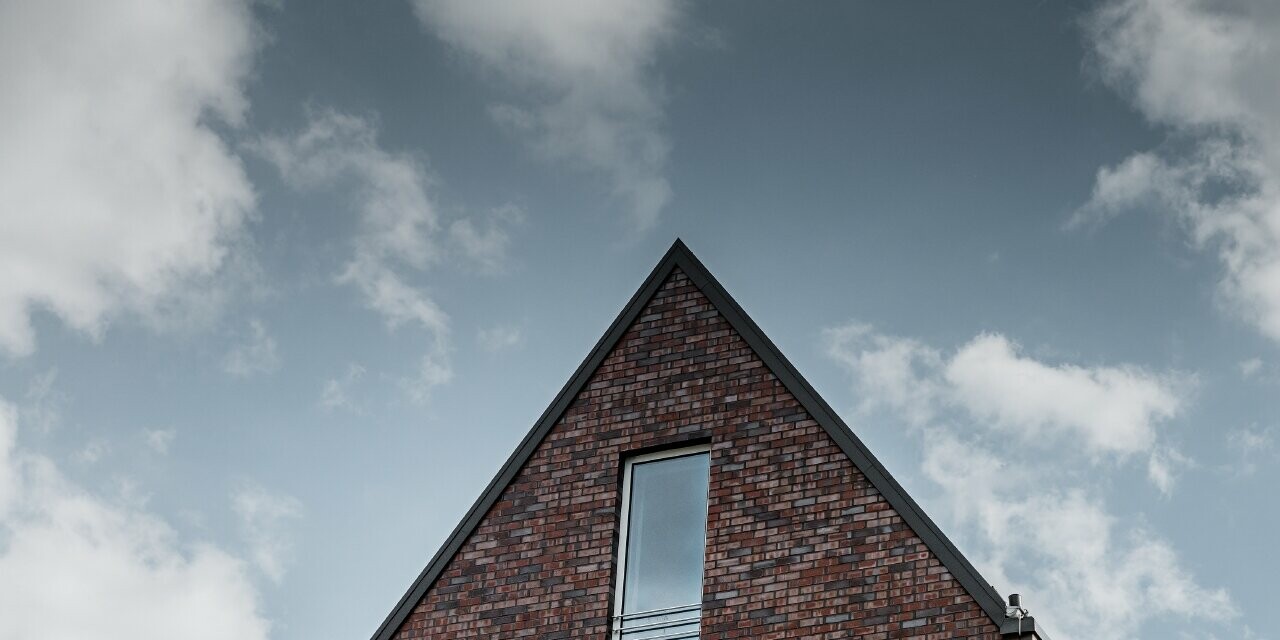 Bâtiment commercial avec façade en brique et grandes surfaces vitrées ; une partie de la façade courbe a été habillée avec le losange de façade doré en aluminium de PREFA.