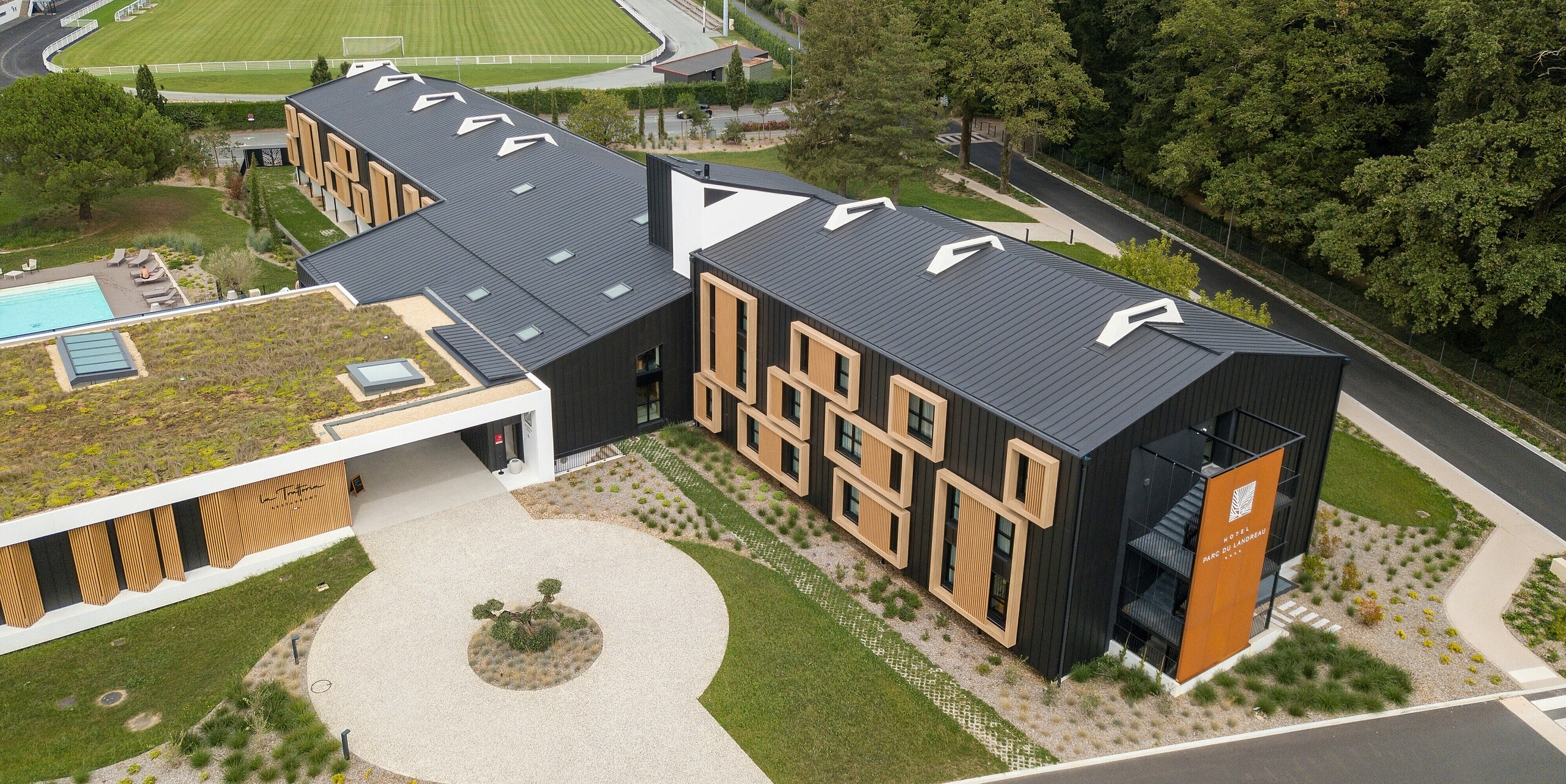 Vue aérienne de l'Hôtel Parc du Landreau aux Herbiers, France, avec une couverture de toit à joint debout uniforme sous forme de PREFALZ en gris noir. Le système de toiture moderne en aluminium impressionne par sa durabilité et sa résistance aux intempéries et s'intègre harmonieusement dans le paysage environnant. Les lignes claires du toit à joint debout complètent parfaitement la conception architecturale du bâtiment.