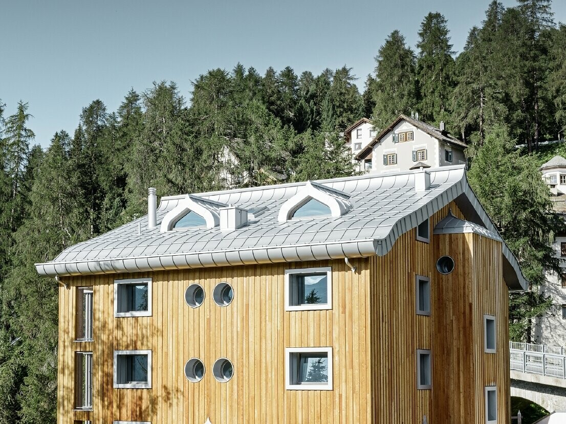 Wohnhausanlage in St. Moritz mit Holzfassade und Aluminiumdach mit geschwungener Traufe in silbermetallic