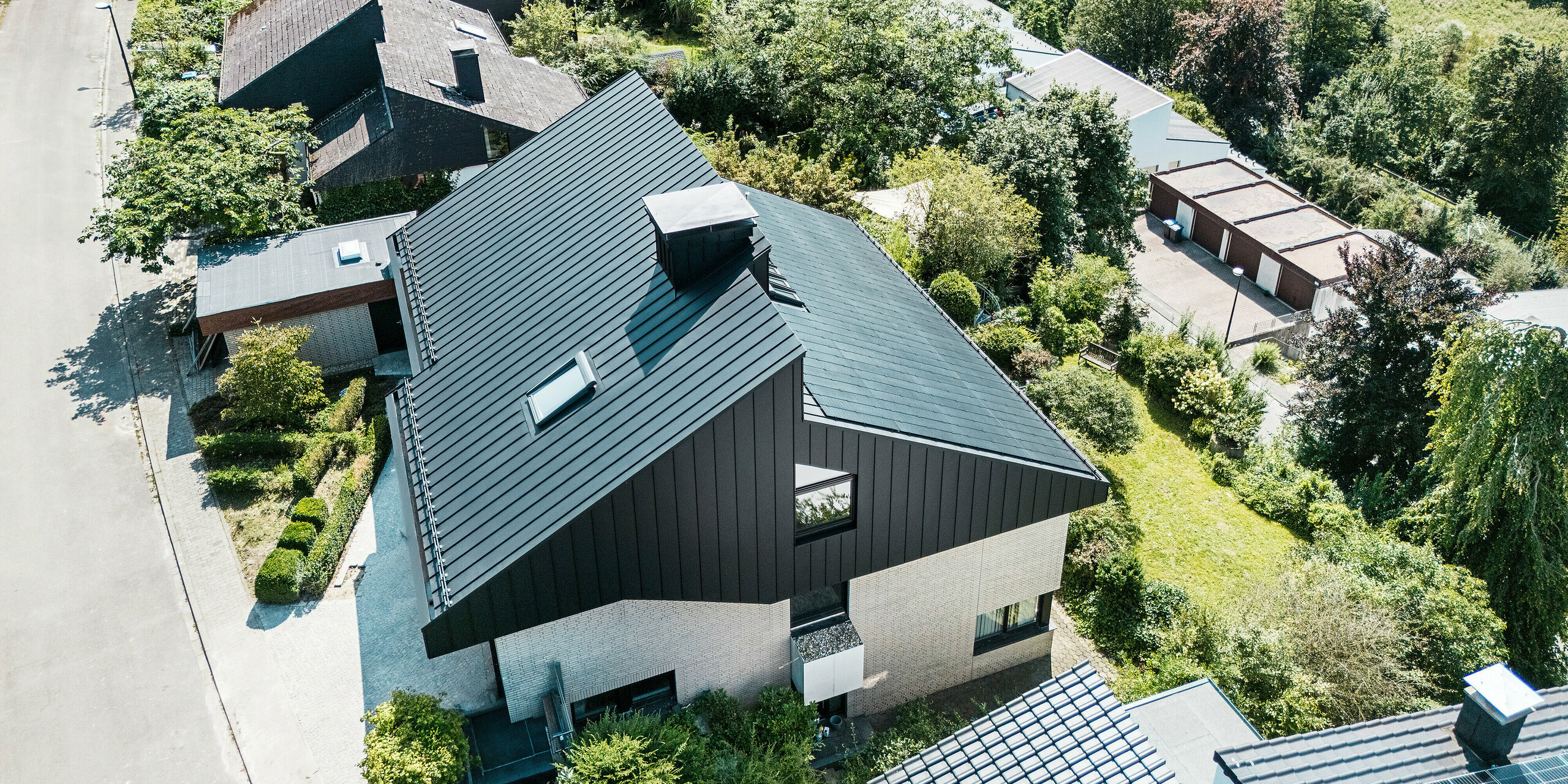 Maison unifamiliale à Meschede, en Allemagne, avec toit en pente décalé et produits innovants en aluminium PREFA. La surface du toit combine un attrayant toit à double joint debout en PREFALZ P.10 noir et des modules photovoltaïques verre/verre sans cadre avec la technologie TOPCon pour une production d'électricité respectueuse de l'environnement à partir d'énergies renouvelables. La façade en aluminium côté pignon et le système de toiture photovoltaïque durable soulignent l'architecture moderne, la fonctionnalité et la durabilité.