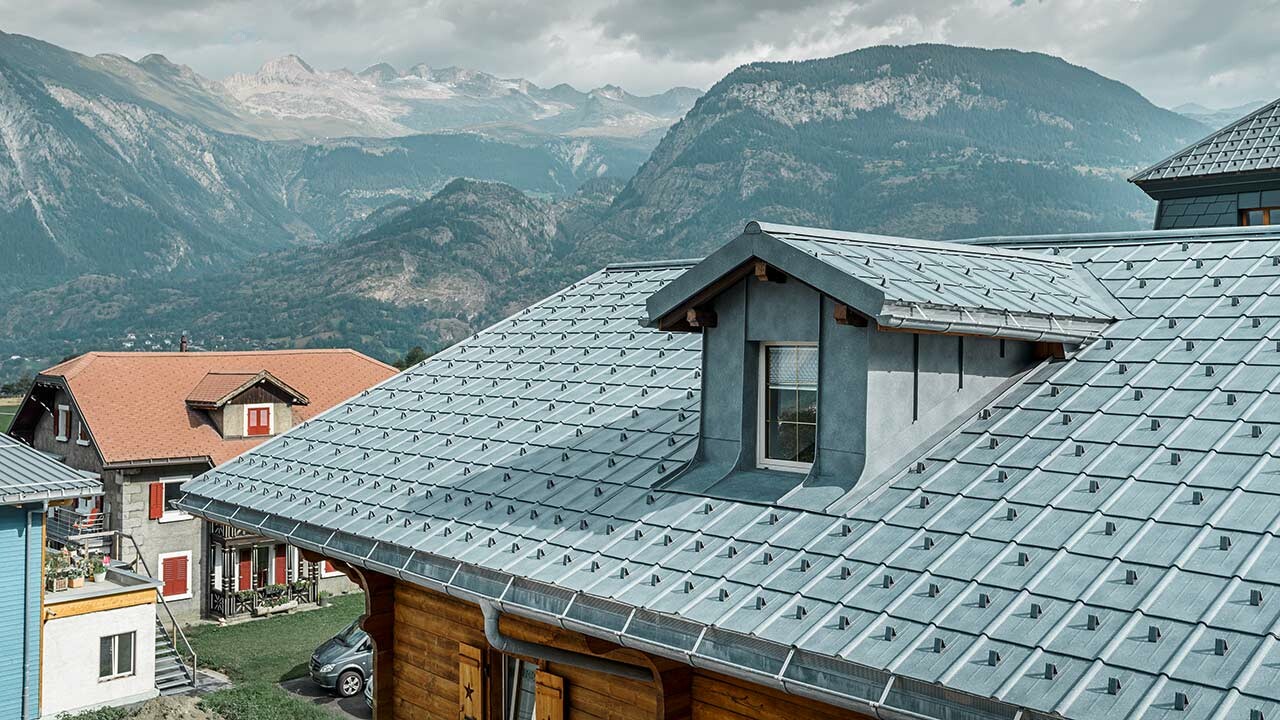 Toit à deux pans avec lucarne ; le choix s’est porté sur la toiture en tôle de PREFA et la tuile couleur gris pierre. La lucarne est habillée d’une couverture à joint debout de PREFA couleur gris pierre.