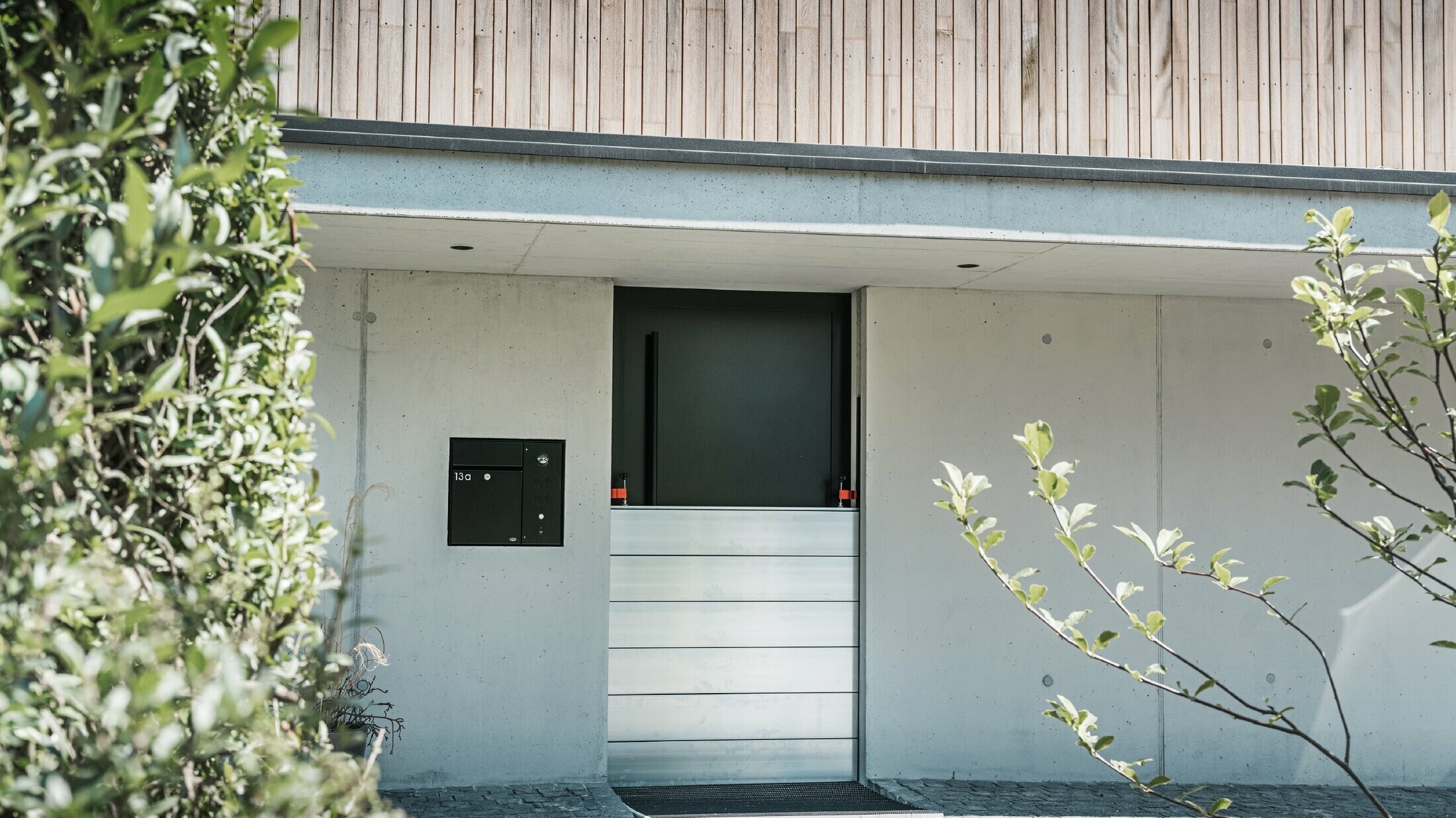 La protection contre les crues PREFA est installée devant la porte d'entrée d'une maison individuelle avec une façade en bois. 