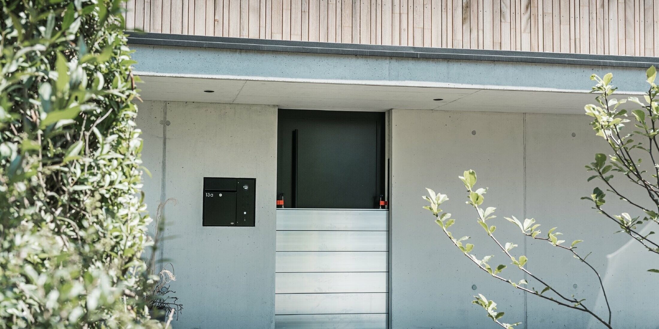 La protection contre les crues PREFA est installée devant la porte d'entrée d'une maison individuelle avec une façade en bois. 