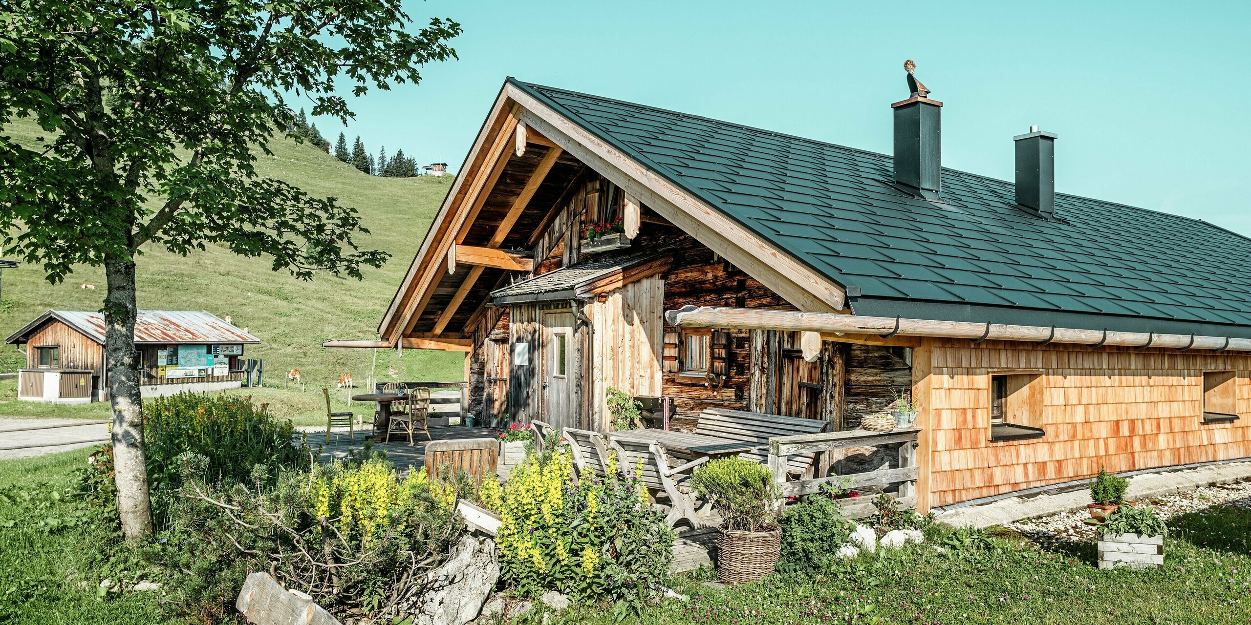 Cabane traditionnelle en bois sur le Walleralm à Bayrischzell avec toit PREFA de haute qualité et système de gouttière. Dans le cadre d'une rénovation de toiture, des panneaux de toiture durables PREFA R.16 de couleur noire P.10 ainsi que des tuiles solaires innovantes PREFA ont été installées. La conception rustique en bois de la cabane s'harmonise avec le drainage du toit unique en bois et en aluminium. Grâce à la rénovation du toit, la cabane combine une technologie solaire économe en énergie avec la protection éprouvée des produits en aluminium robustes de PREFA.