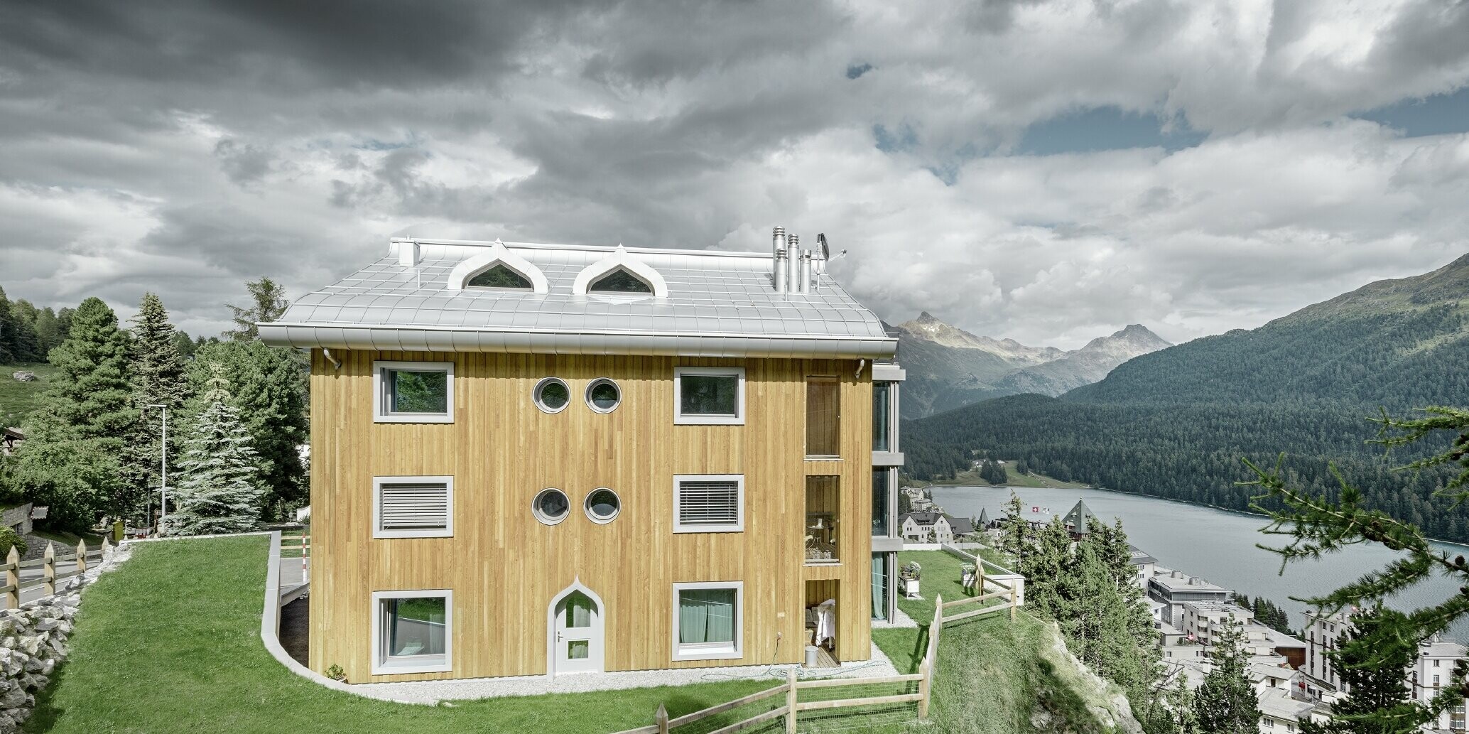 Wohnhausanlage in St. Moritz mit Holzfassade und Aluminiumdach mit geschwungener Traufe in silbermetallic