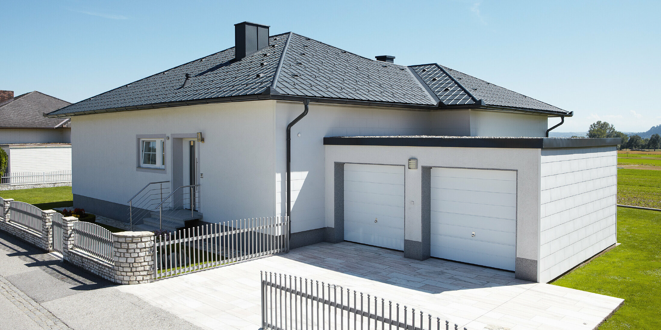 Der neugebaute Bungalow mit Zeltdach wurde mit der PREFA Dachplatte in P.10 Anthrazit eingedeckt. Rechts daneben wurde eine Doppelgarage angebaut, fotografiert wurde von der Straße aus.