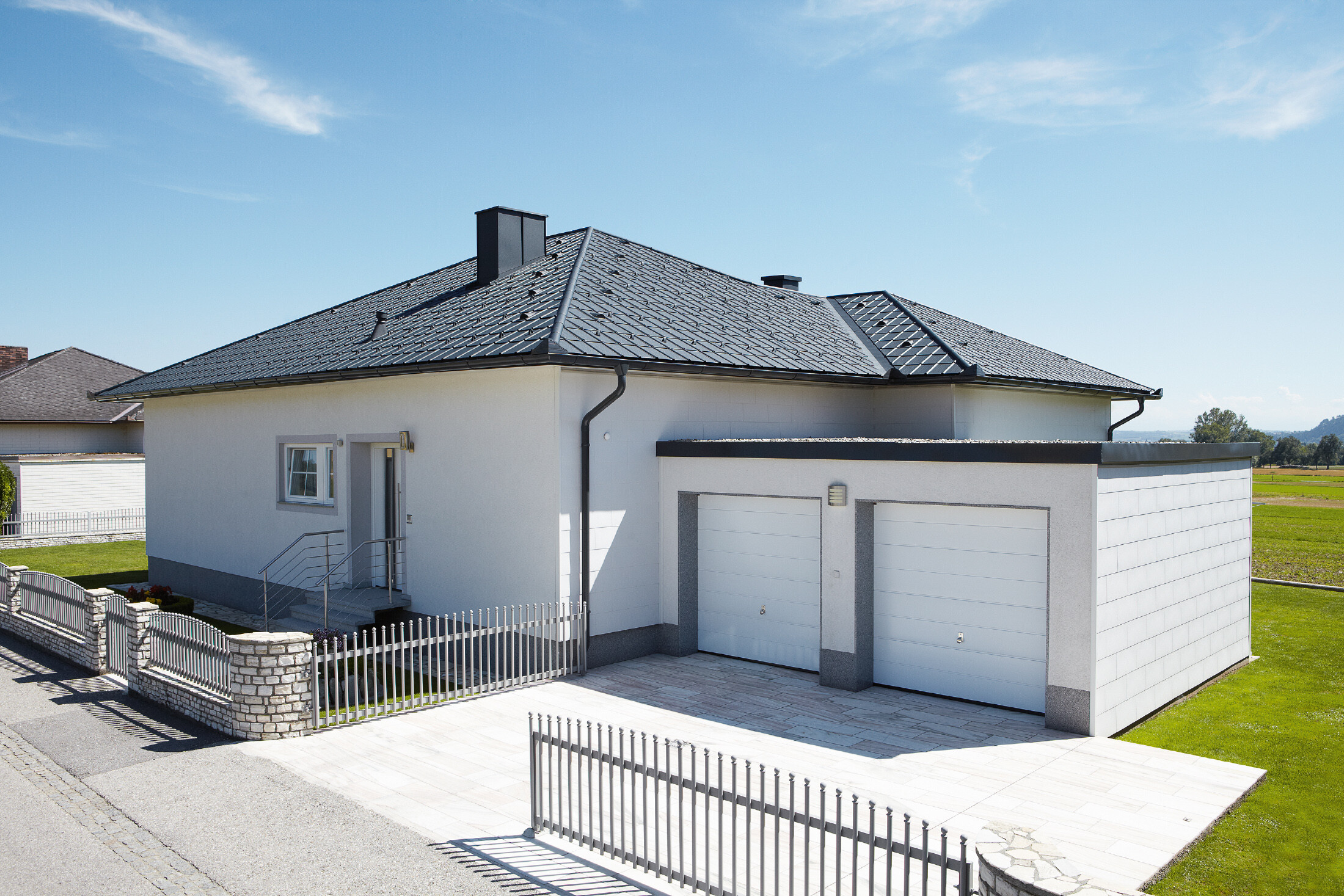 Der neugebaute Bungalow mit Zeltdach wurde mit der PREFA Dachplatte in P.10 Anthrazit eingedeckt. Rechts daneben wurde eine Doppelgarage angebaut, fotografiert wurde von der Straße aus.