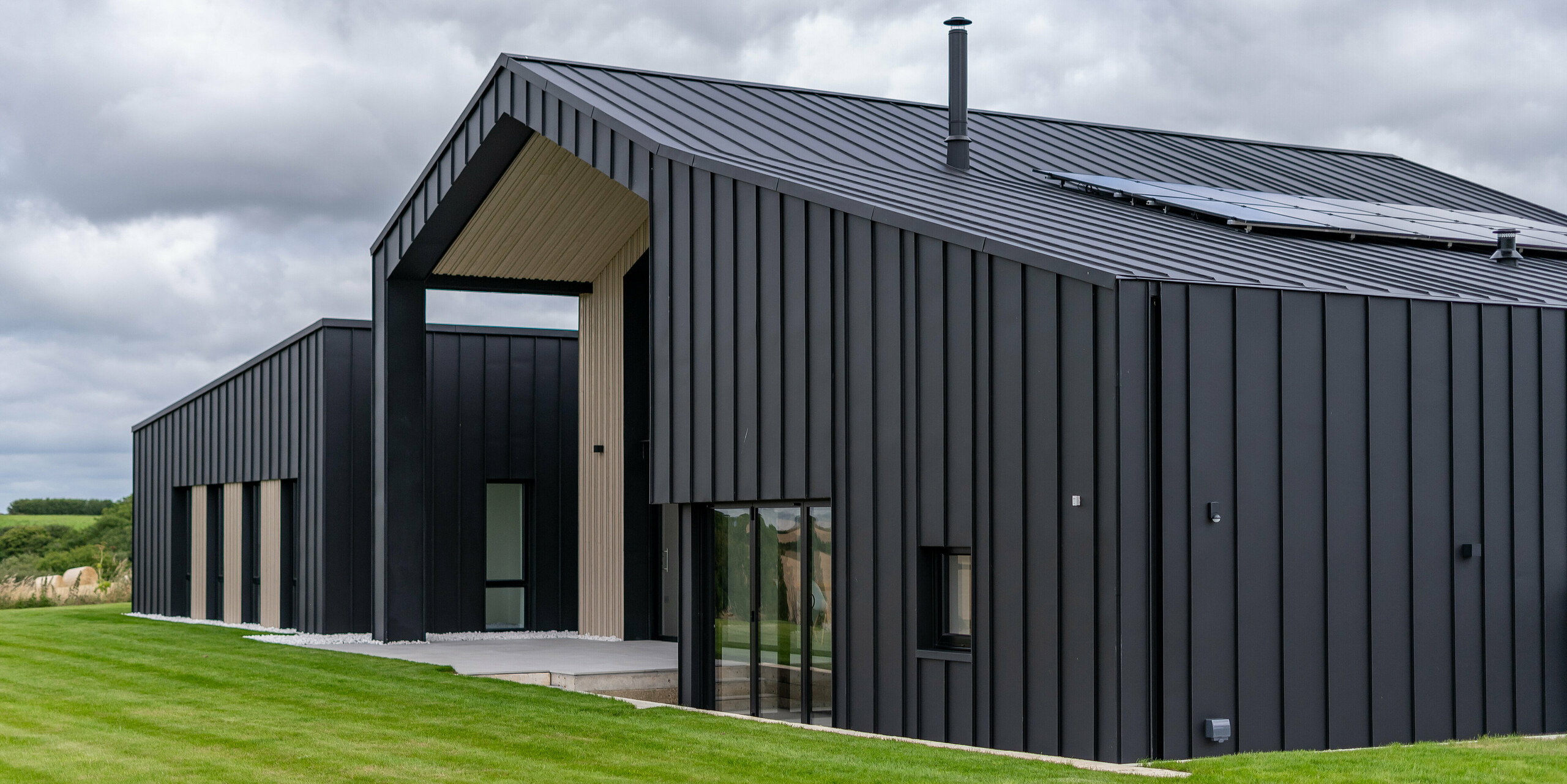 Vue oblique de l'arrière de « The Hide » à Cornwall avec toiture PREFALZ et revêtement de façade en P.10 Anthracite. L'aspect clair des joints debout du toit et de la façade en aluminium crée des lignes modernes et harmonieuses, complétées par des éléments en bois et la nature environnante - une interaction parfaite entre fonctionnalité et esthétique.