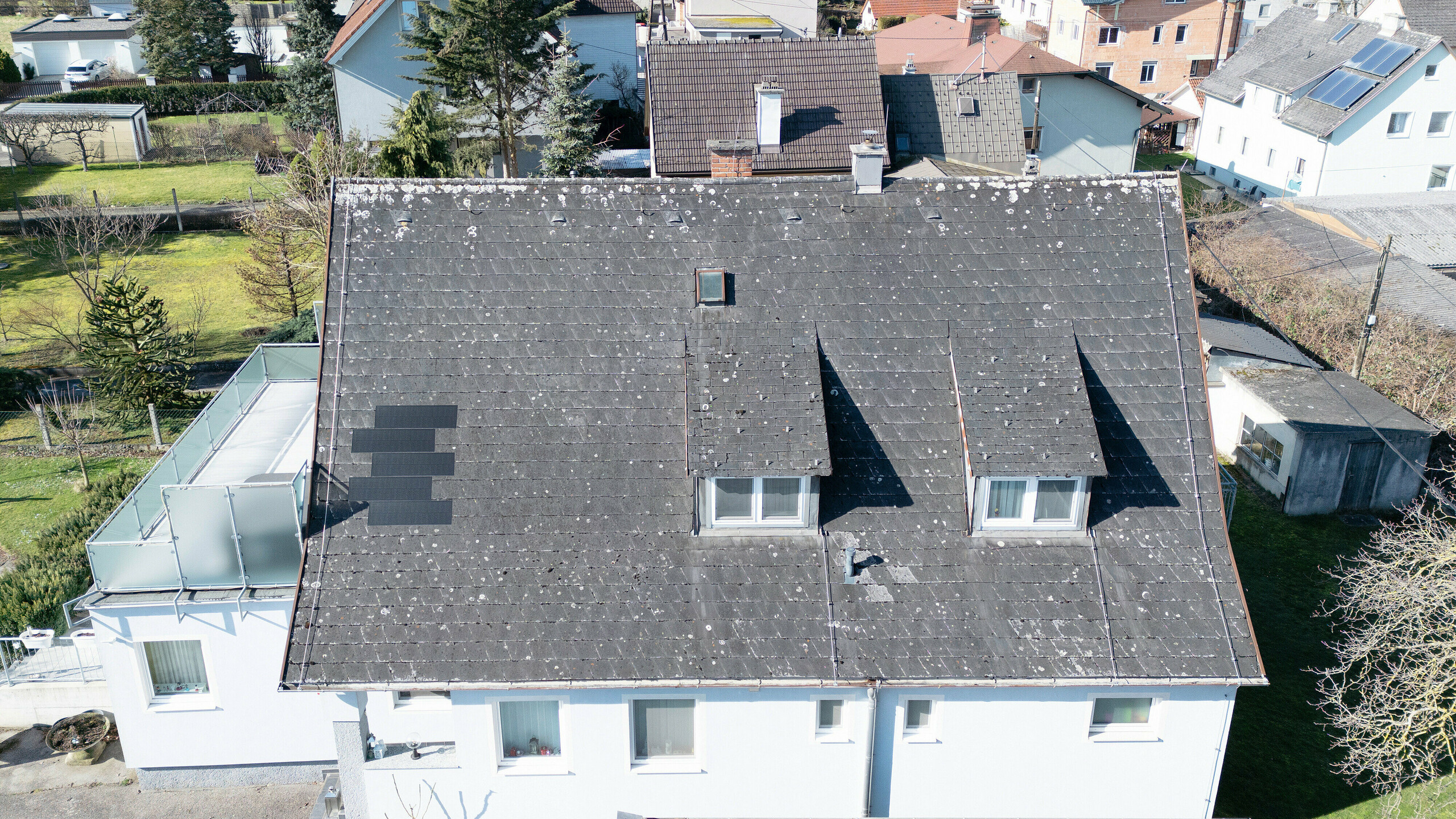 Dach eines Einfamilienhauses in Leonding vor der Sanierung mit PREFA Solardachplatten in Anthrazit. Das Bild zeigt das alte, stark verwitterte Eternit-Dach aus der Vogelperspektive. Die Abnutzung und das Fehlen einer modernen Solaranlage machen eine Dachsanierung notwendig. Dieses Projekt veranschaulicht die Transformation eines alten Dachs in eine nachhaltige und energieeffiziente Lösung mit integrierten Solarmodulen.