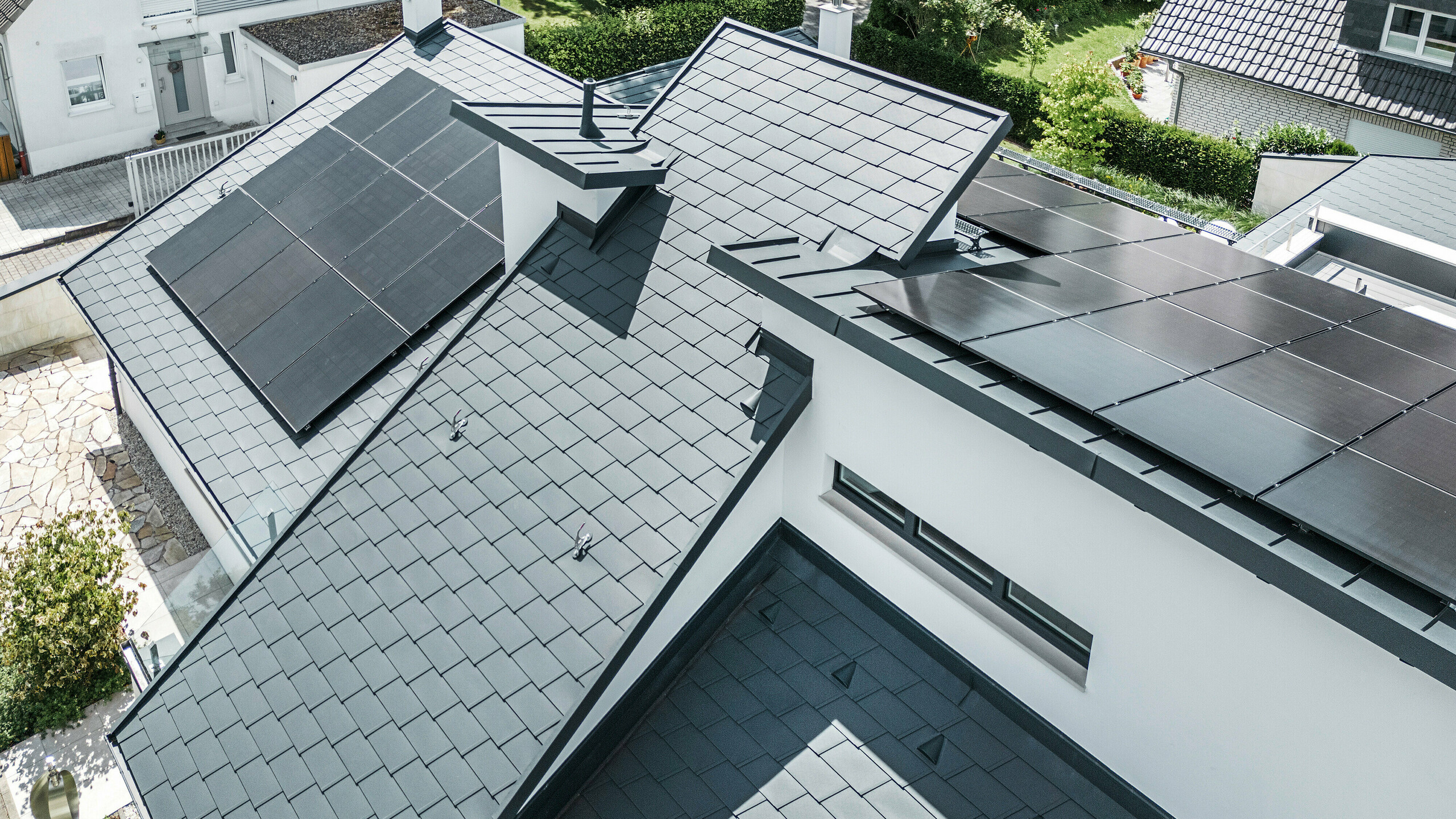 Vue à vol d'oiseau des différents niveaux sur le toit d'une maison individuelle moderne à Dortmund ont été équipés de bardeaux de toit PREFA DS.19 et PREFALZ de couleur P.10 anthracite ainsi que d'une installation photovoltaïque de grande surface.
