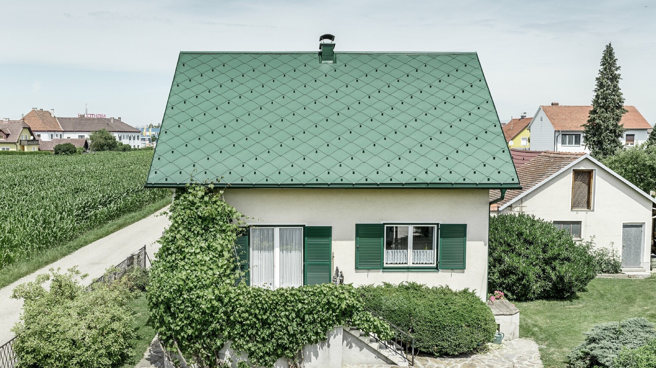 Toit à pignon de maison individuelle classique avec couverture en aluminium vert mousse et volets verts Le toit est recouvert de losanges de toiture PREFA 44 × 44 en P.10 vert mousse.