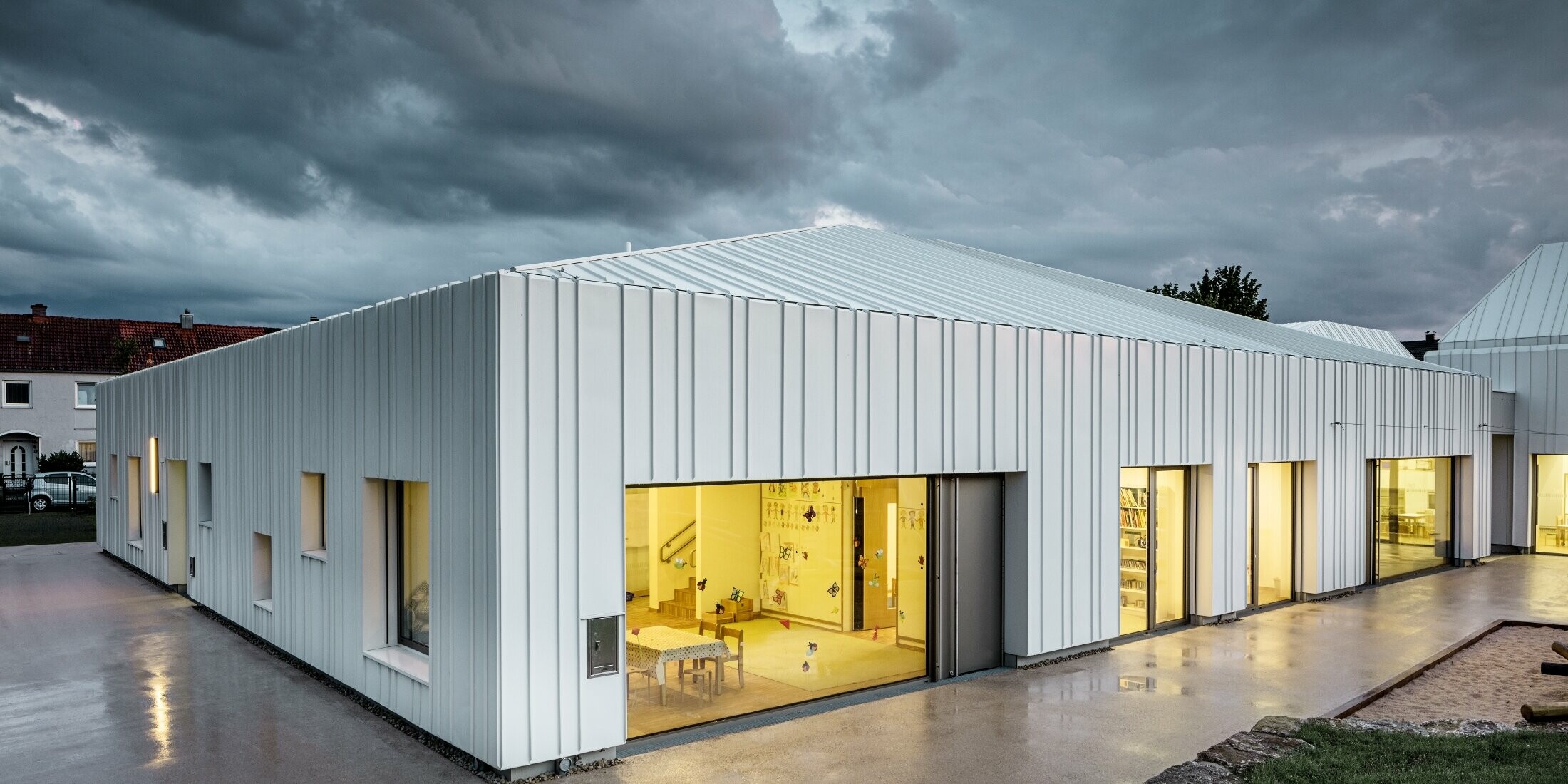 Crèche à Niederwerrn avec toit et façade PREFALZ dans la couleur blanc pur, avec différentes largeurs de bac, photographiée au crépuscule dans des conditions nuageuses