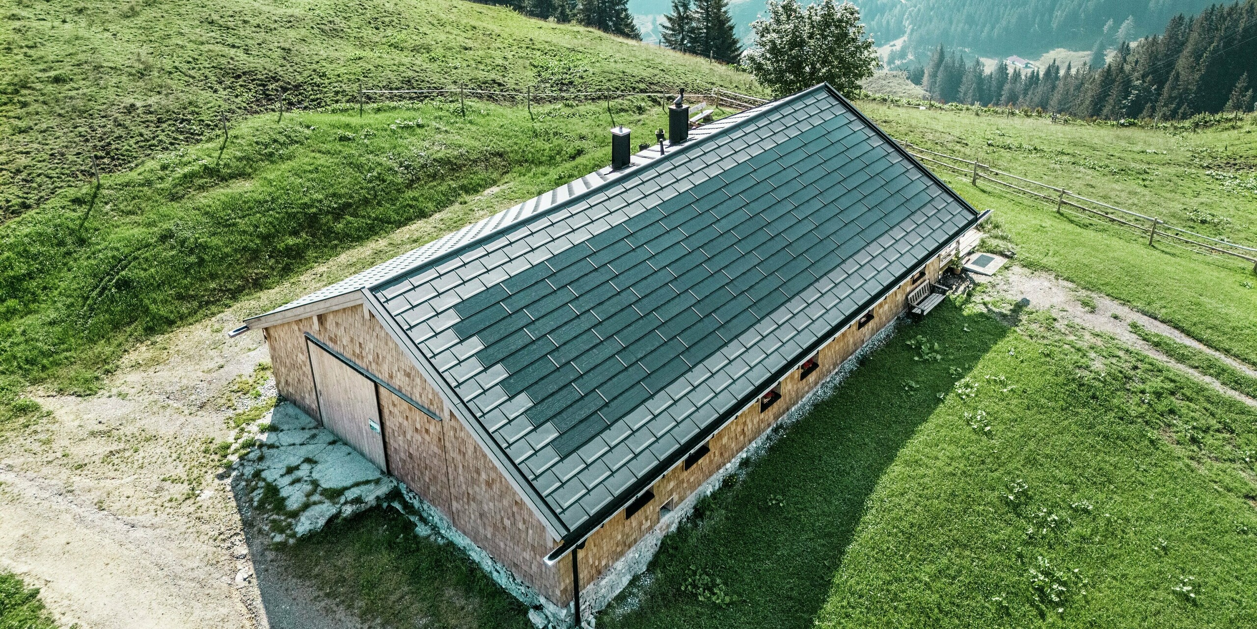 Prise de vue par drone de la Birkehütte sur le Walleralm à Bayrischzell au milieu d'un paysage de montagne idyllique. Lors de la rénovation, le toit a été équipé de panneaux de toiture durables PREFA R.16 en noir P.10 et de tuiles solaires innovantes PREFA. Cette solution moderne associe la production d’énergie durable à la protection robuste des produits en aluminium PREFA éprouvés et s’intègre harmonieusement dans l’environnement alpin.