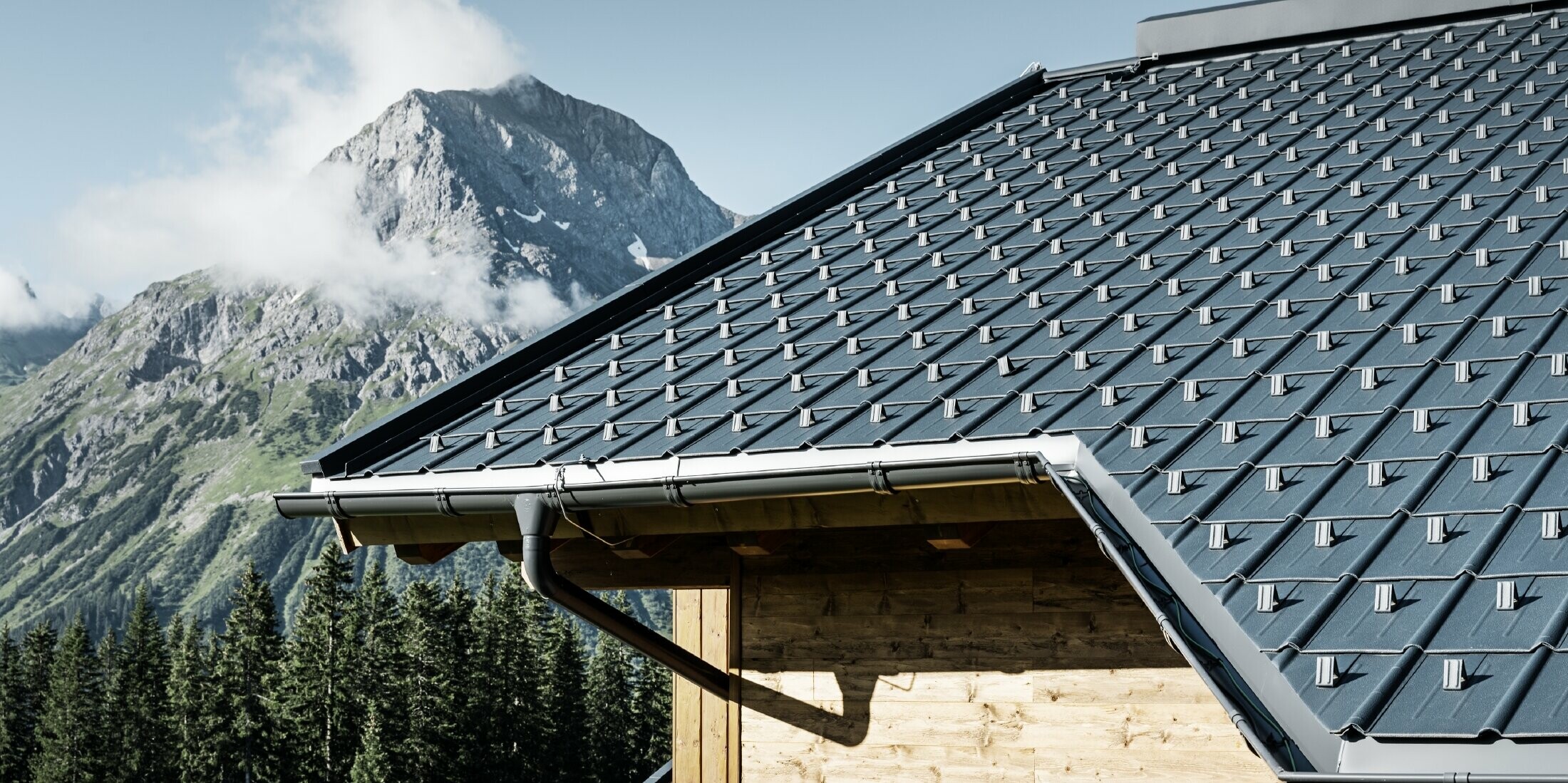 Maison en bois à la montagne, la toiture est recouverte avec la tuile PREFA couleur anthracite avec gouttière PREFA et façade en bois