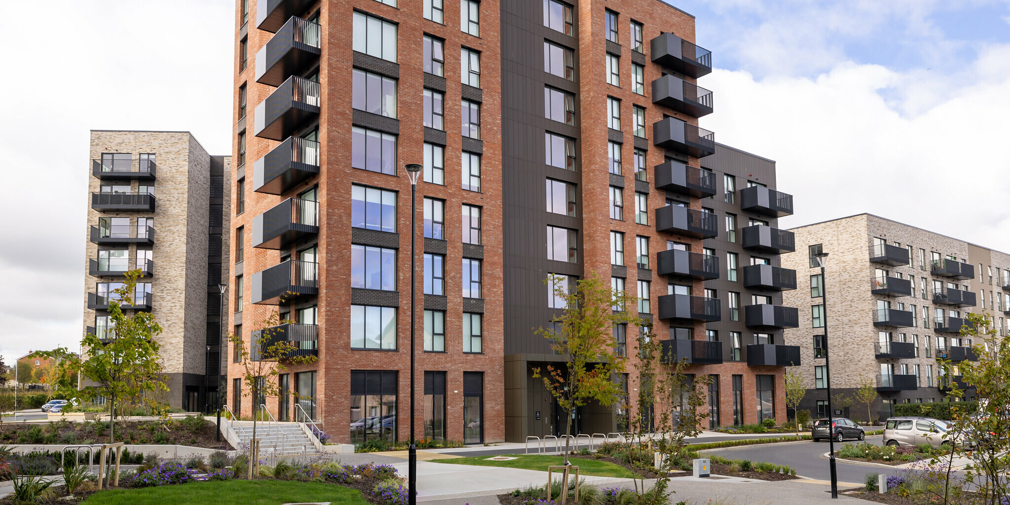 Vue de face des Citywest Apartments à Dublin. L'immeuble résidentiel associe une façade traditionnelle en briques à un design moderne composé de parements PREFA posés verticalement en P.10 brun. Des balcons spacieux et des fenêtres généreuses soulignent l'architecture moderne. D'une superficie d'environ 700 m², la façade en aluminium résistante aux intempéries offre une solution élégante et durable qui s'intègre harmonieusement dans l'environnement urbain avec son espace vert bien entretenu.