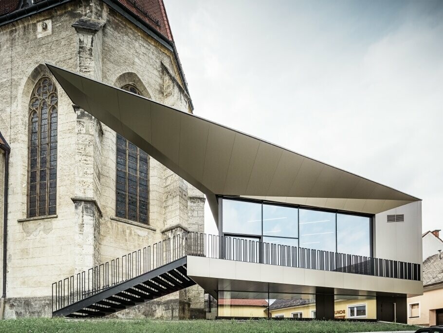 Seitliche Ansicht auf das Pfarrzentrum FOKUS mit PREFA Fassade und die Kirche in Sierning (AT).