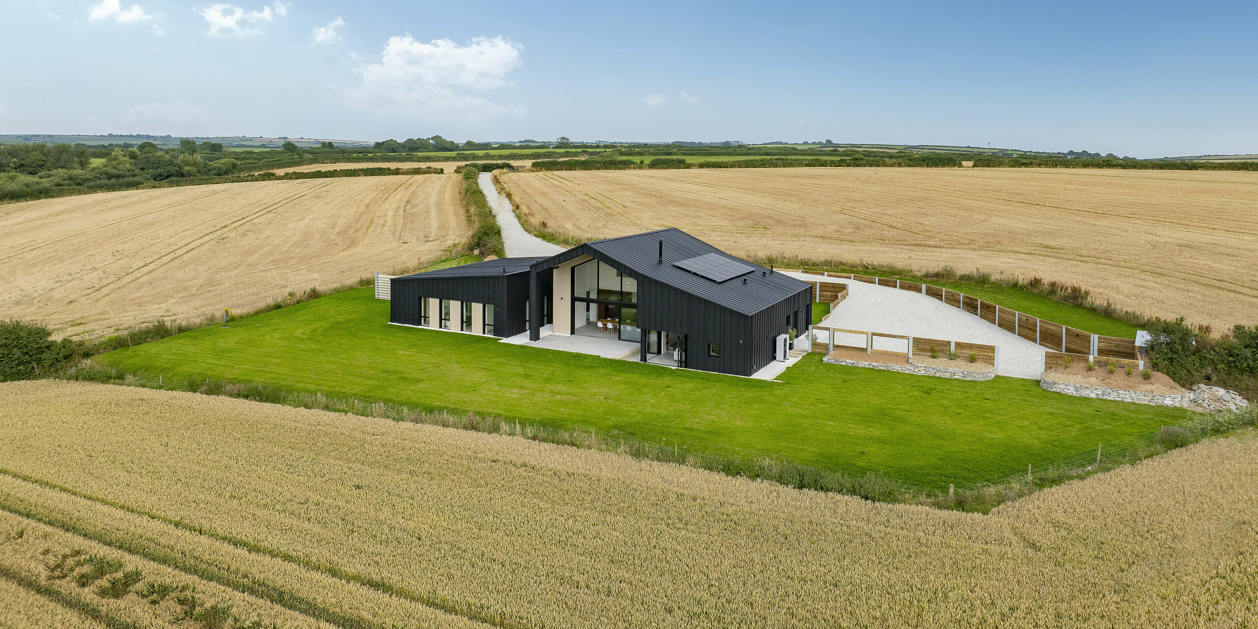 Vue panoramique depuis « The Hide » en Cornouailles, niché dans des champs ouverts. Devant la maison il y a un espace vert bien entretenu. La maison familiale moderne impressionne par sa coque en aluminium PREFALZ de couleur anthracite avec le revêtement éprouvé P.10. La toiture et la façade s'harmonisent parfaitement avec l'environnement naturel. L'aspect clair des joints debout confère au bâtiment élégance et durabilité.