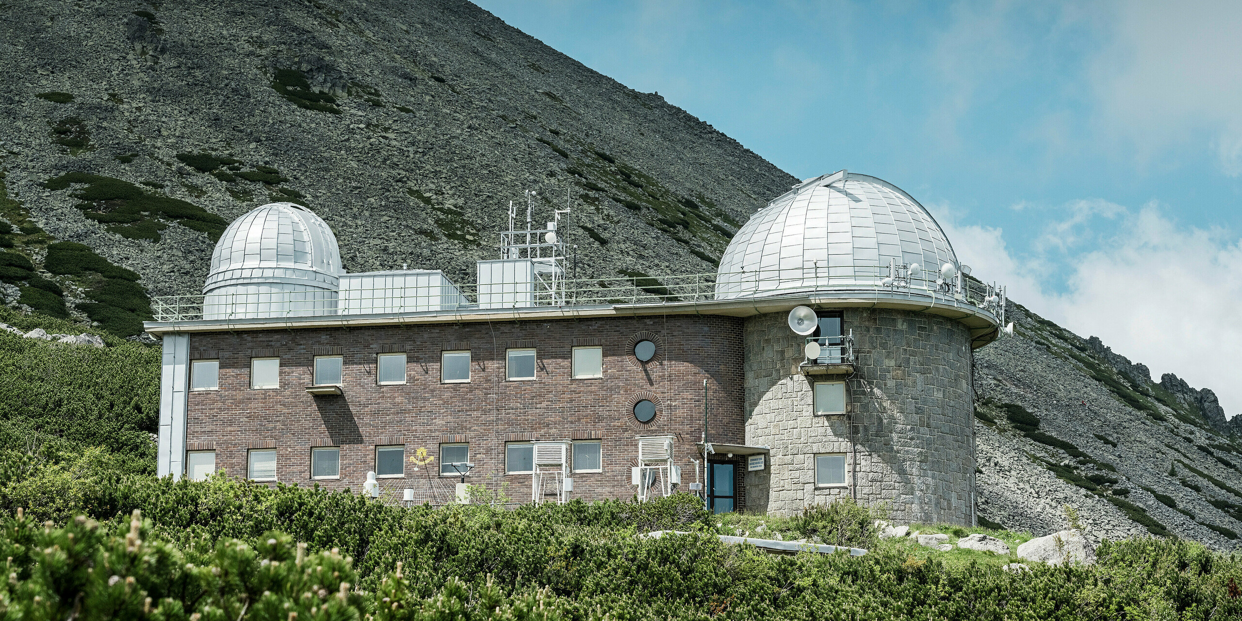 Das Observatorium in Skalnate Pleso, eingebettet in die natürliche Berglandschaft der Hohen Tatra, zeigt stolz seine glänzenden PREFALZ Aluminiumkuppeln in Silbermetallic. Die strukturelle Kombination aus dauerhaftem Stein, traditionellem Ziegel und modernen Aluminiumelementen bildet einen kontemplativen Kontrast zur rauen Bergwelt. Dieses historische Observatorium steht als Wächter über die weiten Ebenen der Slowakei und ist ein Symbol für die Verbindung von Wissenschaft und Beharrlichkeit.