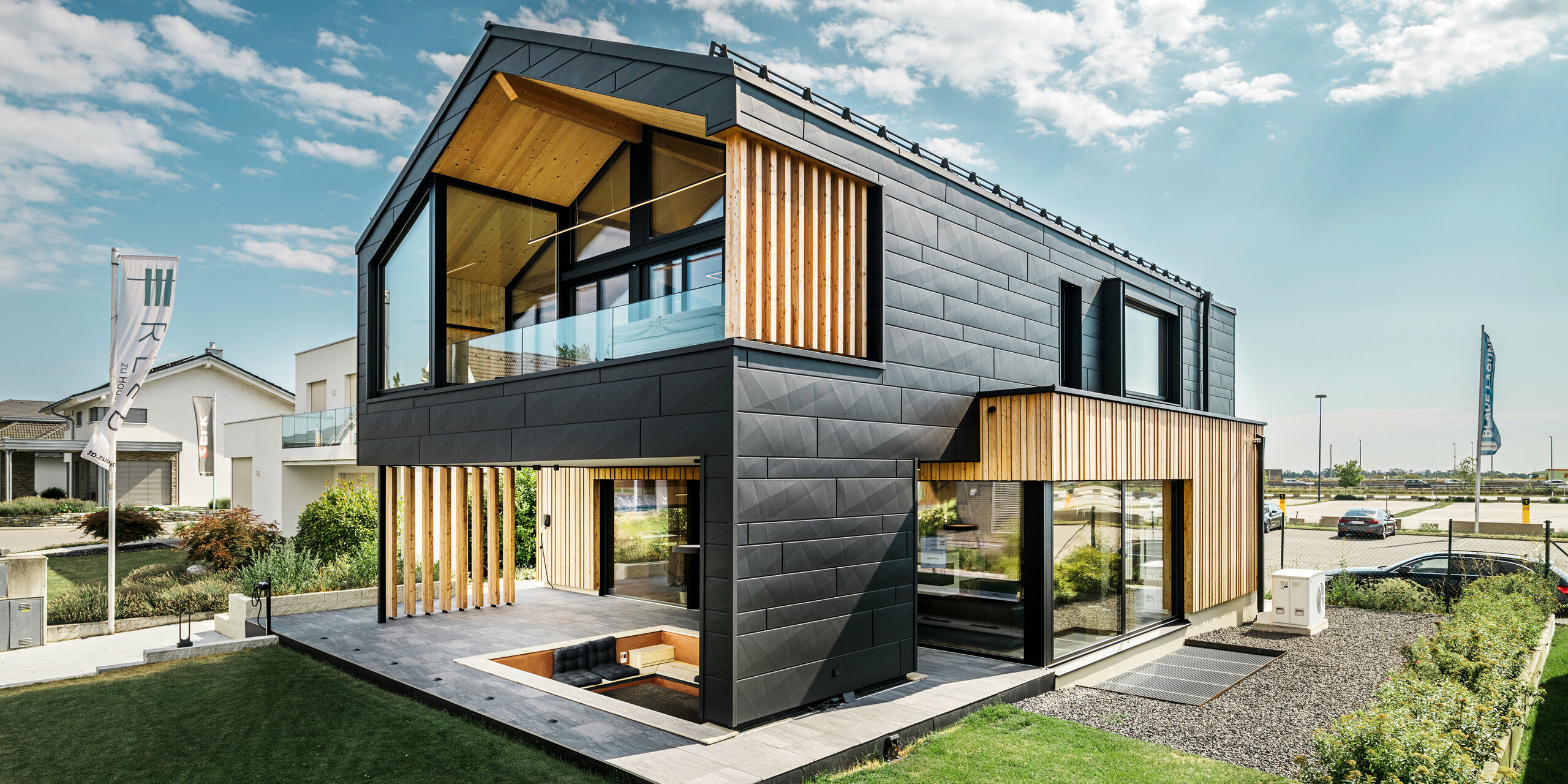 La maison modèle Autark du centre de maisons préfabriquées Blaue Lagune à Vösendorf (AT) présente une combinaison moderne de panneaux de façade PREFA Siding.X en P.10 noir et d'éléments en bois naturel. La grande loggia et le balcon s'intègrent harmonieusement dans le design contemporain. Les éléments en bois créent une atmosphère accueillante et la façade robuste en aluminium assure durabilité et résistance aux intempéries. Le jardin spacieux avec terrasse et coin salon intégré complète le concept architectural extraordinaire et durable.