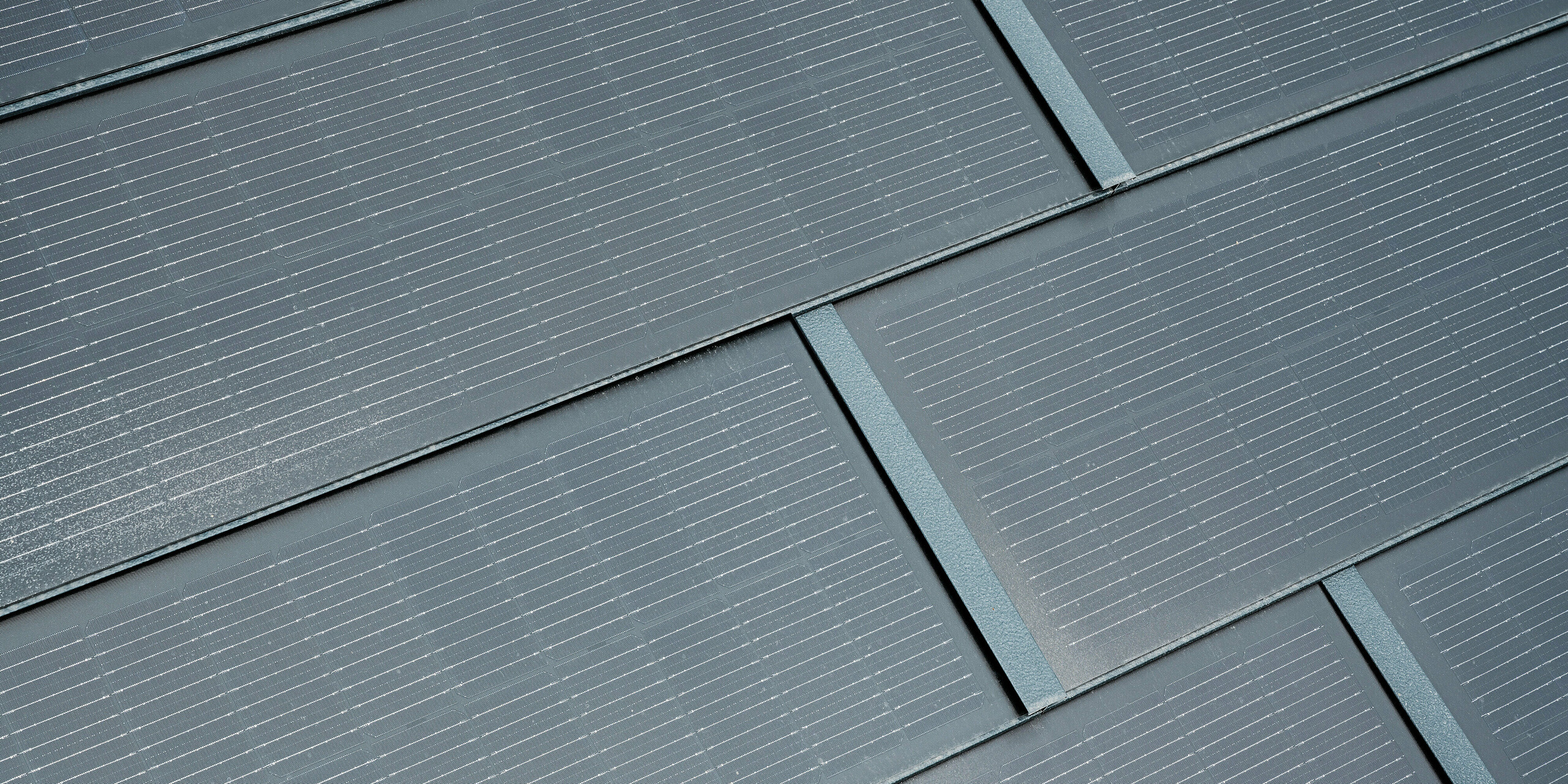 Prise de vue en détails des tuiles solaires PREFA en anthracite. Les lignes fines des cellules solaires sont clairement visibles et s'intègrent harmonieusement dans le design global. Cette intégration attrayante de la technologie solaire dans la toiture allie fonctionnalité et esthétique moderne, fournissant ainsi une source d’énergie respectueuse de l’environnement pour les bâtiments.