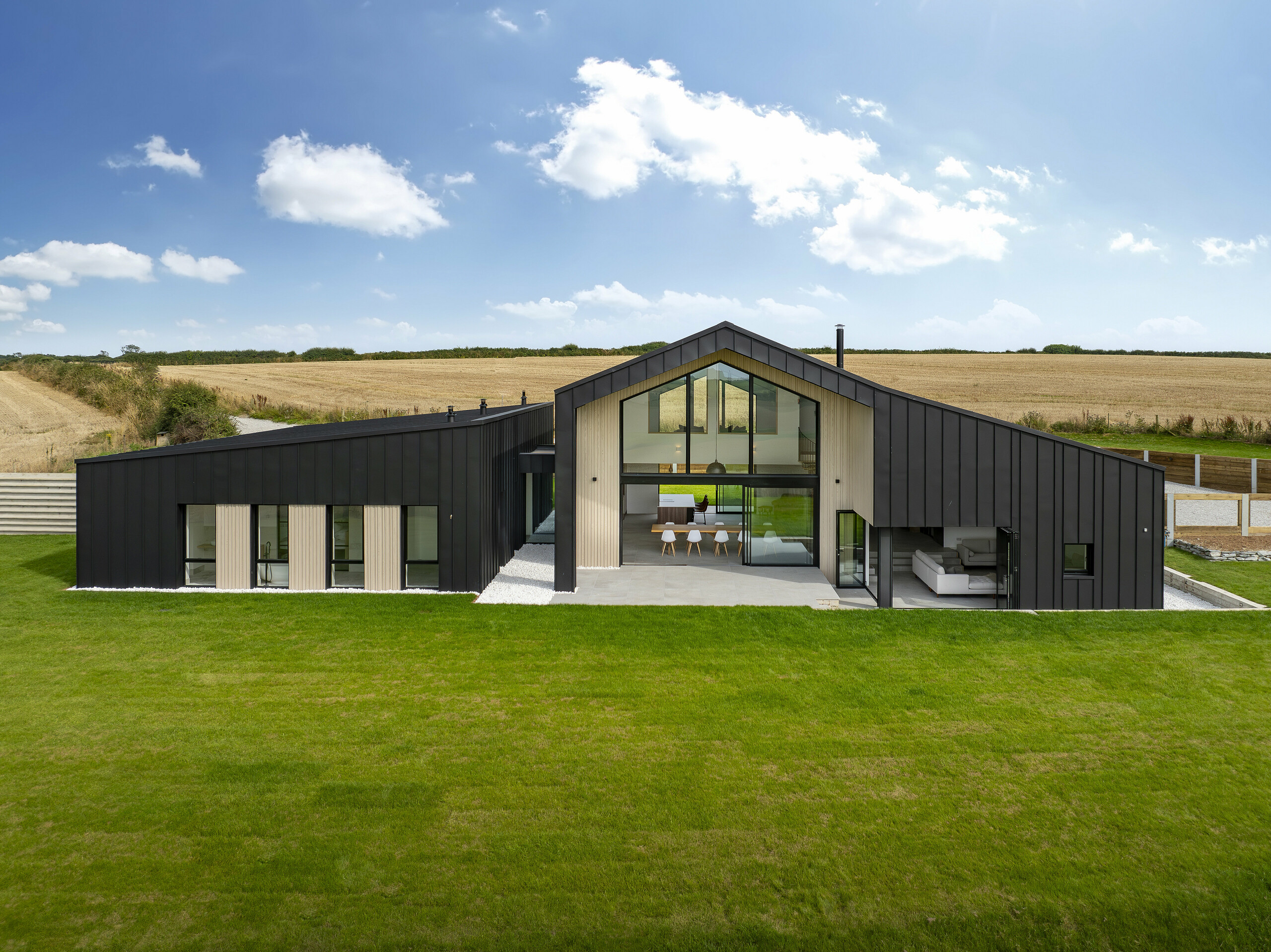 Vue frontale de l'arrière de « The Hide » à Cornwall. La généreuse façade vitrée, encadrée par un revêtement en aluminium PREFALZ en P.10 anthracite, ouvre l'intérieur sur le spacieux jardin. L'aspect clair des joints debout associé à des éléments en bois naturel souligne le design moderne et harmonieux.