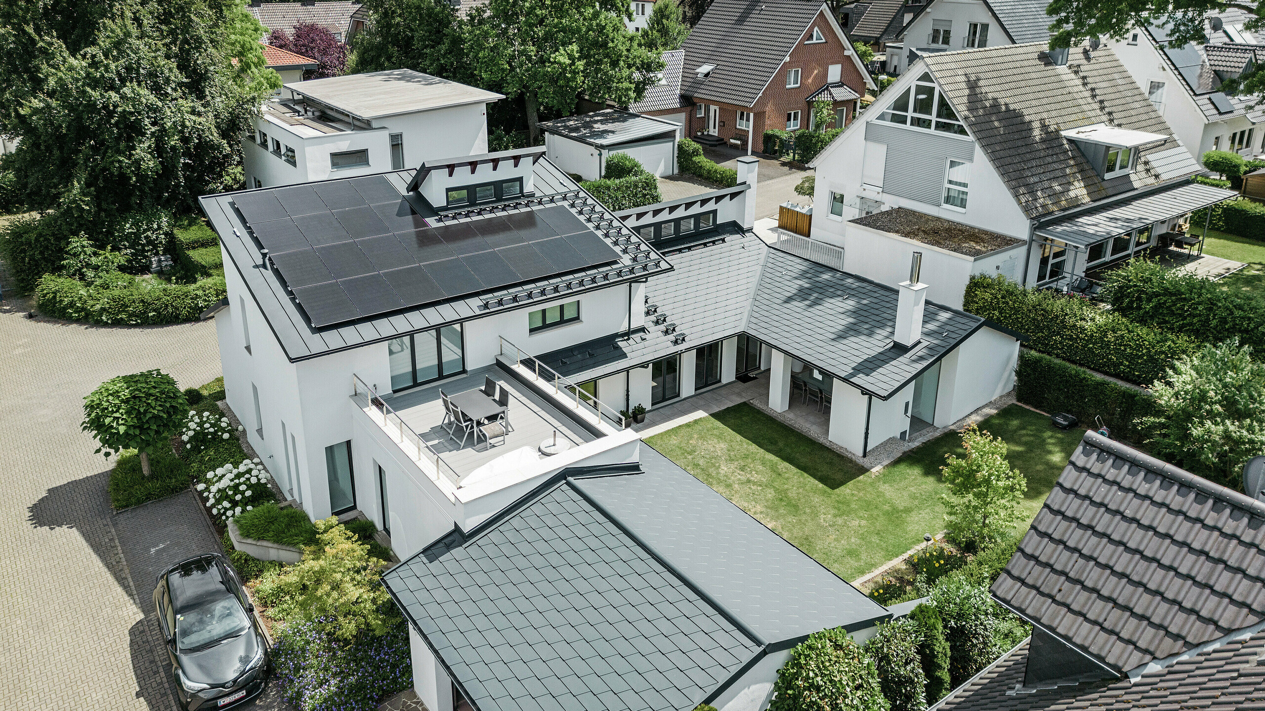 Vue aérienne du paysage de toit exceptionnel d'une maison individuelle à Dortmund avec des bardeaux PREFA DS.19 et PREFALZ en P.10 anthracite ainsi qu'une installation PV de grande surface.