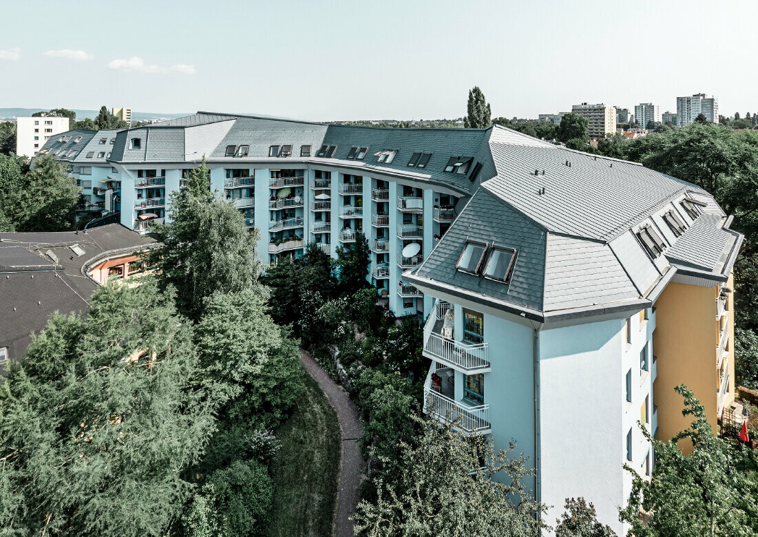 Grand bâtiment d’habitation consacré à l’accueil des personnes âgés, recouvert de bardeaux de toiture et Prefalz PREFA couleur gris pierre, avec de nombreux balcons.