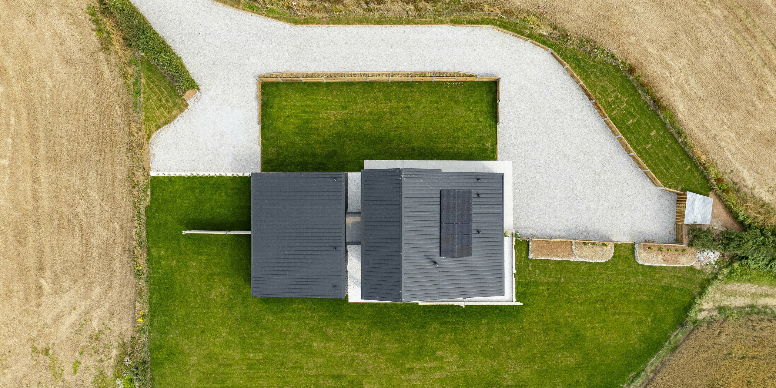 Vue aérienne de « The Hide » en Cornouailles, encadrée par des prairies bien entretenues et des champs ouverts. Le toit en aluminium PREFALZ en P.10 anthracite se caractérise par des lignes claires et une finition précise, associées à des panneaux solaires durables. L'installation photovoltaïque fournit de l'électricité à partir d'énergies renouvelables. Le design moderne s'intègre harmonieusement dans l'environnement idyllique et offre une vue plongeante impressionnante.