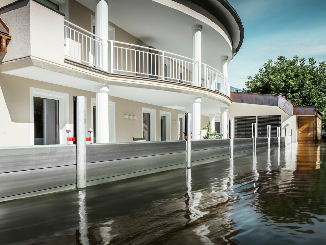 On voit ici une maison individuelle avec balcon. Grâce à la protection contre les crues PREFA, la maison est protégée de la montée des eaux qui a déjà commencé.