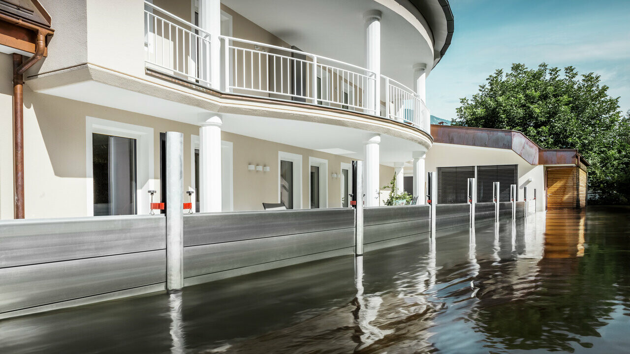 On voit ici une maison individuelle avec balcon. Grâce à la protection contre les crues PREFA, la maison est protégée de la montée des eaux qui a déjà commencé.